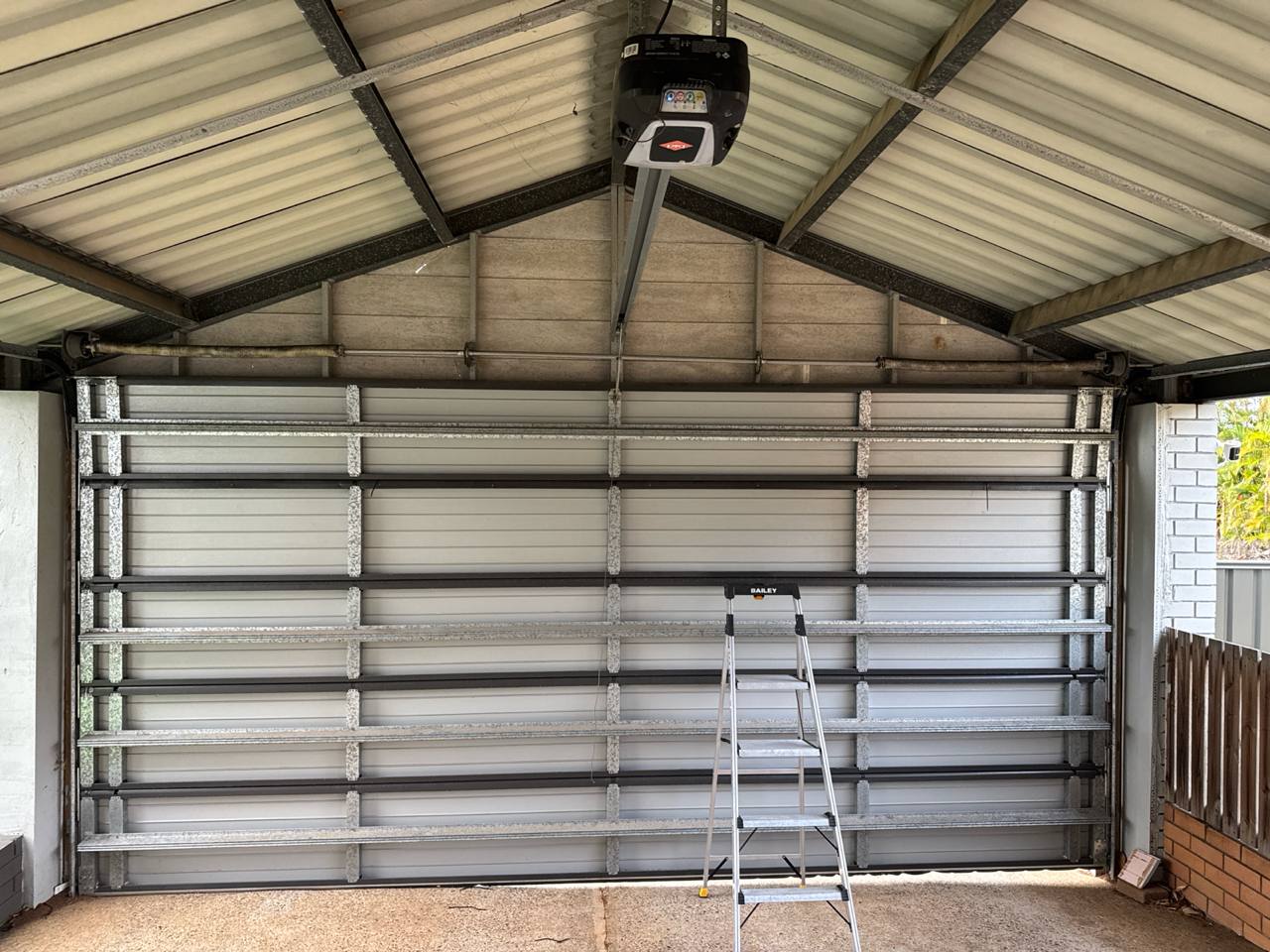 Interior view of a B&D sectional garage door with horizontal panels and bracing, a step ladder positioned in front, and an automatic opener mounted to the ceiling ridge in Kallangur, Brisbane.