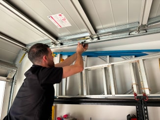 Technician performing garage door repair by adjusting a metal bracket on the garage door mechanism, with a ladder visible in the background.