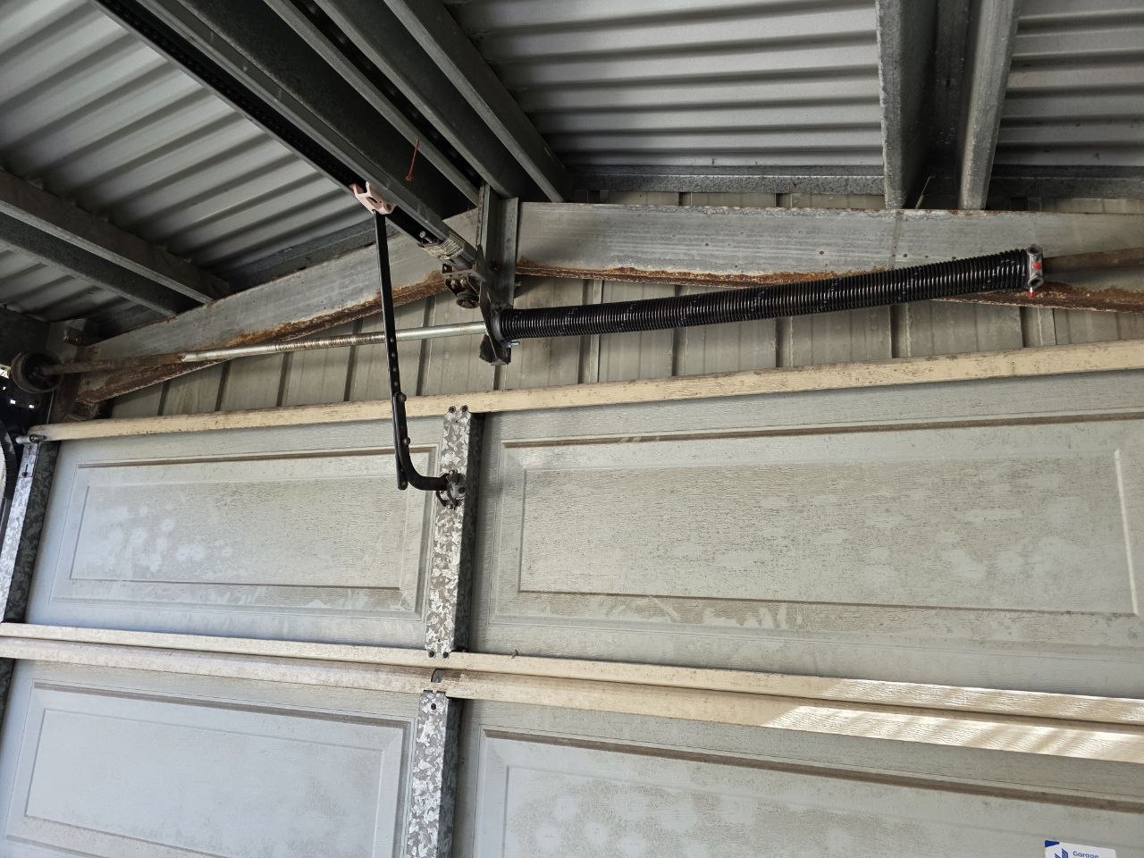 Newly installed black torsion spring mounted above a sectional garage door with the door arm bracket visible below in Bundoora, Melbourne.
