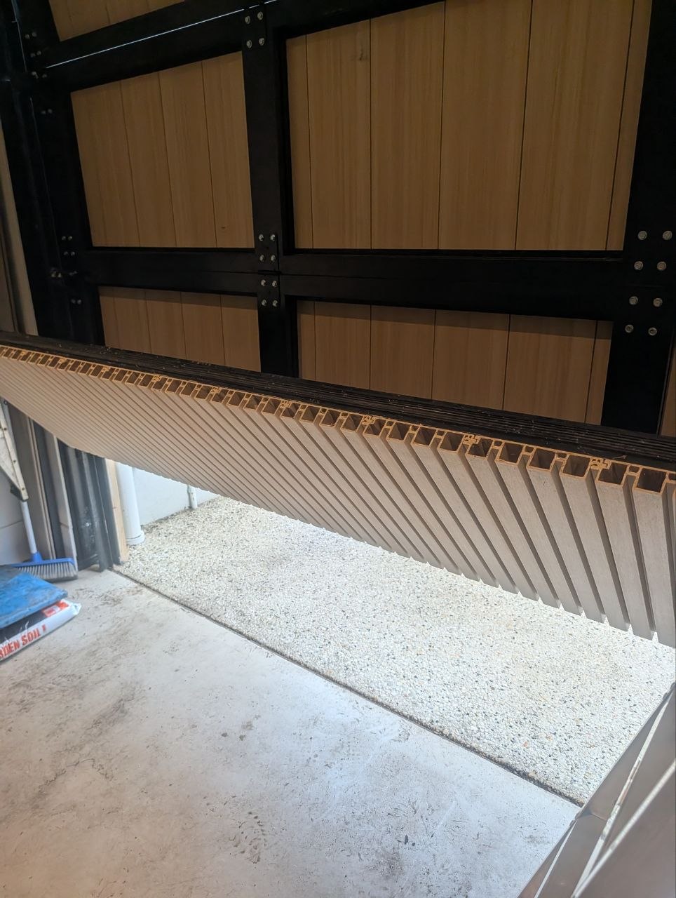 Underside view of a sectional door with the bottom panel displaced and hanging away from the door frame, exposing the hollow-core panel profile in Elwood, Melbourne.
