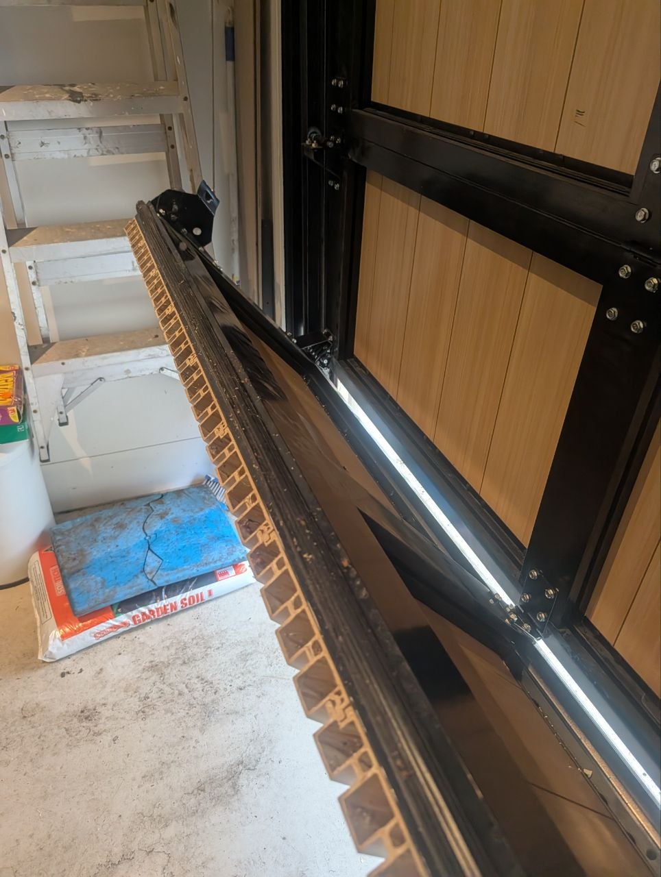 Side view of a sectional door showing a gap between the misaligned bottom panel and the vertical track during a realignment job in Elwood, Melbourne.
