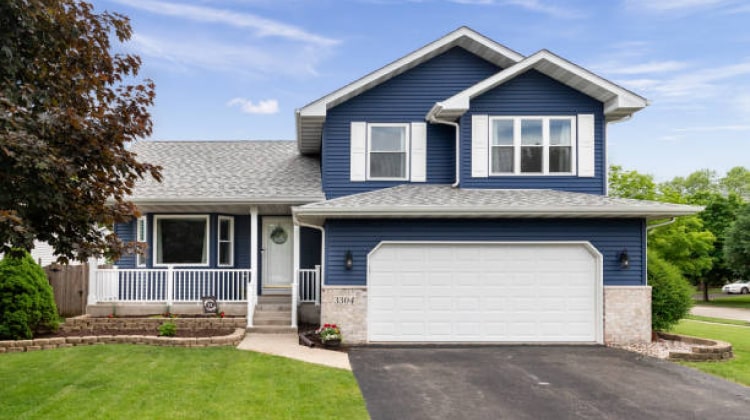 A modern suburban home with a blue exterior and a white garage door, featuring a well-maintained lawn and driveway.
