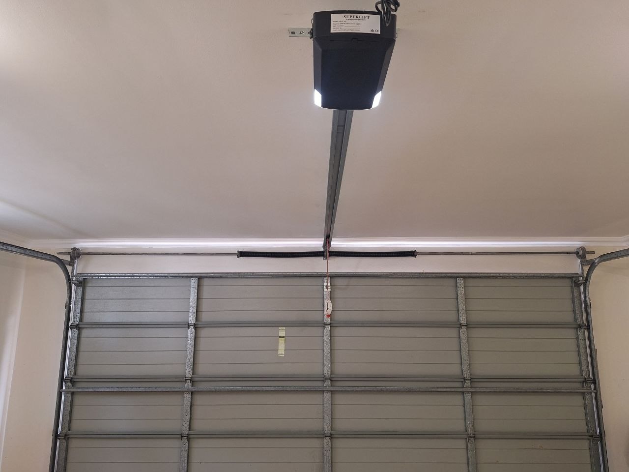Superlift garage door motor mounted on the ceiling with a torsion spring and drive rail above a residential sectional garage door in Merrimac, Gold Coast.